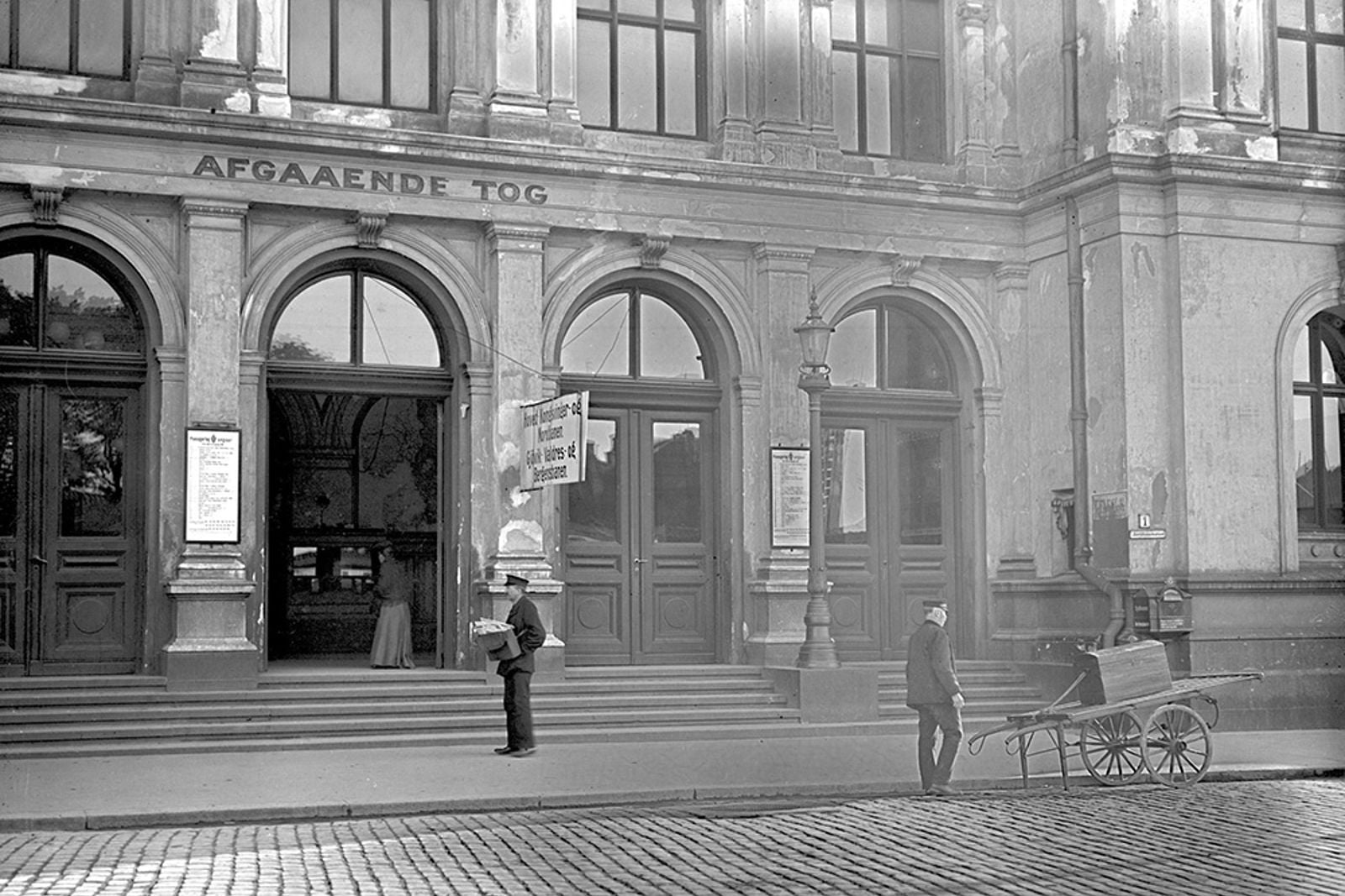 Trapper og inngangsdører. To menn i uniform, den ene med håndkjerre.